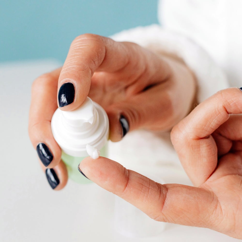 Hands holding a bottle of Copper Peptide Daily Moisturizer and pumping a small amount onto the tip of the finger to demonstrate usage.