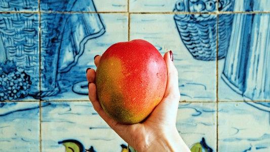 A woman's hand holding a mango, African Mango has been shown to help control appetite by regulating leptin production.